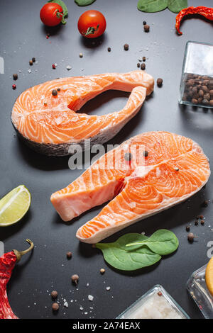 Zwei frische rohe Lachssteaks mit Salz, Pfeffer, Zitrone auf schwarzen Hintergrund. Stockfoto