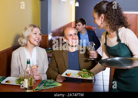 Lächelnde Kellnerin mit älteren Gästen Paar am Tisch im Restaurant Stockfoto