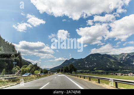 Autobahn oder Landstraße mit einer Brücke in den Bergen mit klaren Kennzeichnung durch pulsierende grüne Bäume unter blauem Himmel umgeben. Stockfoto