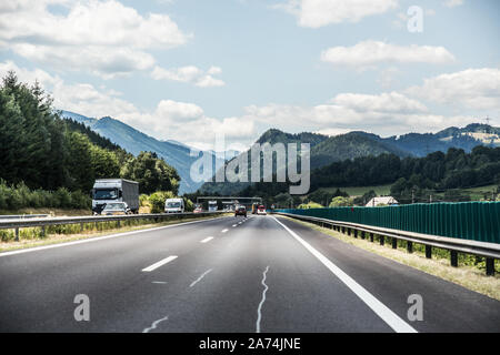 Autobahn oder Landstraße mit einer Brücke in den Bergen mit klaren Kennzeichnung durch pulsierende grüne Bäume unter blauem Himmel umgeben. Stockfoto