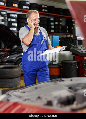 Professionelle reife Mechaniker in der Werkstatt, um am Telefon für sie notwendige Ersatzteile Stockfoto