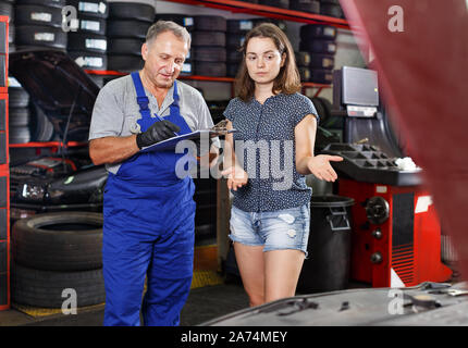 Professionelle männlichen Mechaniker diskutieren mit weiblichen Client und Aufnahme Liste der Werke auf Auto Reparatur in einer Werkstatt Stockfoto