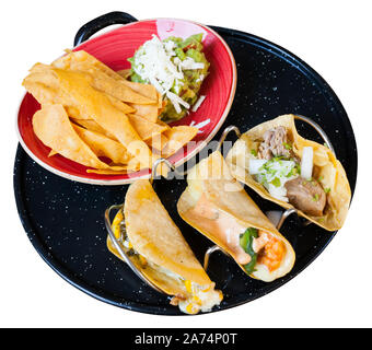 Traditionelle mexikanische Tacos mit verschiedenen Füllungen serviert mit Guacamole und nachos Chips. Auf weissem Hintergrund Stockfoto