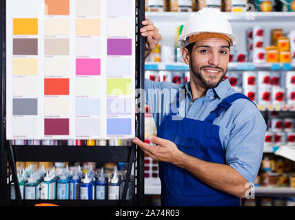 Gewöhnliche Vorarbeiter in blauen Overalls mit Proben von Farbe auf Stand in Store Stockfoto