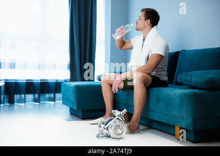 Jungen gutaussehenden Mann Trinkwasser aus der Flasche während des Trainings zu Hause leben sportlich Stockfoto