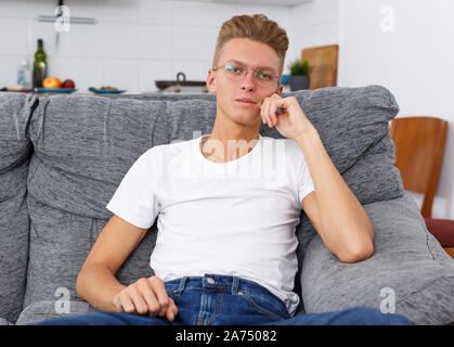 Portrait von gutaussehenden blonden jungen Kerl in Freizeitkleidung auf dem Sofa zu Hause Stockfoto