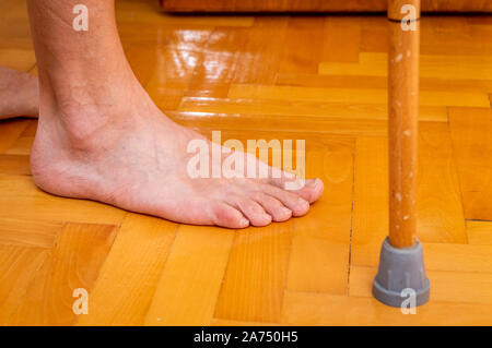 Nahaufnahme der Barefoot behinderter Mann mit einem Stock auf dem Parkettboden. Behinderung Konzept. Stockfoto