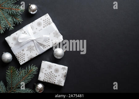 Geschenkboxen verpackt Silber Papier und Tannenbaum Äste mit dekorativen Kugeln über schwarzen Hintergrund. Weihnachten banner Mockup, Neues Jahr Postkarte Vorlage Stockfoto