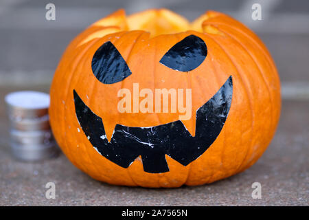 Lächelnd orange Halloween Kürbis auf dem Boden liegend zusammen mit einigen Teelichter im Hintergrund. In Deutschland, in Bayern, im Oktober. Stockfoto