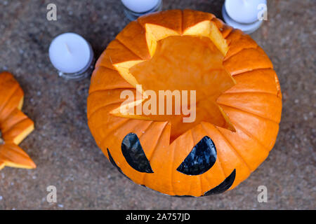 Lächelnd orange Halloween Kürbis auf dem Boden liegend zusammen mit einigen Teelichter im Hintergrund. In Deutschland, in Bayern, im Oktober. Stockfoto