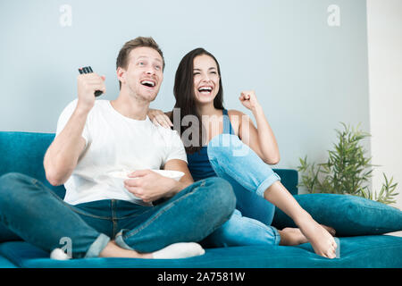 Junges Paar schöne Brünette Frau und gutaussehenden Mann Beifall auf ihre Lieblingsmannschaft während der Fußball Spiel essen Popcorn zu Hause gemütliche Lebensstil Stockfoto