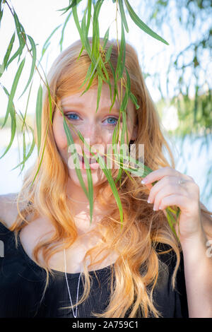Porträt einer wunderschönen Lächeln junges Mädchen mit roten Haaren im Freien Verstecken hinter Blätter