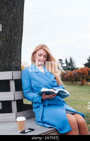 Blonde Frau mit Buch im Herbst Park Stockfoto