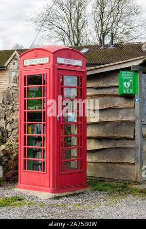 Traditionelle rote Telefonzelle mit einem Defibrillator und buchen Austausch von der Bushaltestelle im Dorf Priddy, Mendip, Somerset, England, Großbritannien, Großbritannien Stockfoto