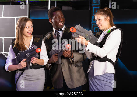 Afrikanischer Mann und zwei hübsche kaukasischen Frauen holding Laser Gewehren und auf der Laser tag Zimmer posing Stockfoto