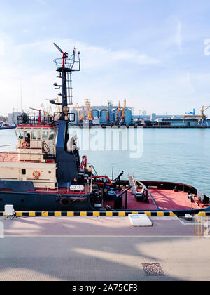 Tugboat auf einem Pier im Hafen behilflich, cargo Sea Port über das Meer, schwebenden Lastkran, Getreidespeicher Aufzüge, Hafen, Boote und Kräne. Industrielle sce Stockfoto