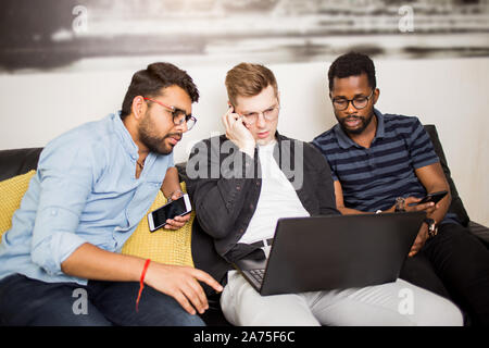 Junge Unternehmer suche Ideen für Business, mit Laptop und Smartphone, Aufruf zu potenziellen Kunden oder Partnern. Multi-ethnische Freunde sitti Stockfoto