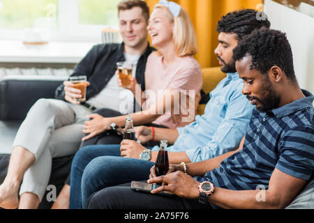 Freundschaft, Freizeit, Erholung, Home Party Konzept. Freunde Fernsehen zu Hause und trinken Bier sitzen auf der Couch im Wohnzimmer. Sport und Unterhaltung Stockfoto
