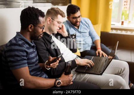 Gruppe freudiger multiethnischen Studenten sitzen auf der Couch am Bildschirm des Laptop suchen, Beobachten, Film oder die Präsentation zusammen. Freunde arbeiten Stockfoto