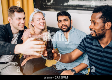 Fröhlich multikulturellen Freunde Studenten legere Kleidung trinken, klirrenden Flaschen und Gläser Getränke, feiert Geburtstag. Drei Mann und woma Stockfoto