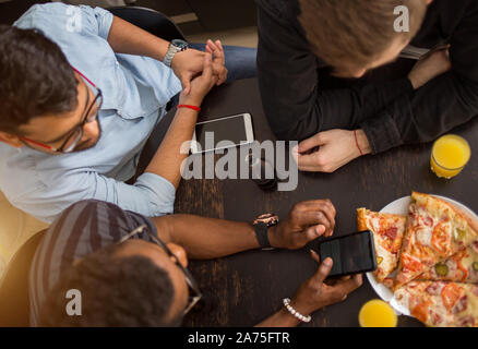 Blick von oben auf die Gruppe der multirassischen Freunde sitzen um den Tisch, Mittagessen, essen Pizza, Saft trinken, über Handy. Lieferung, Essen, Technol Stockfoto