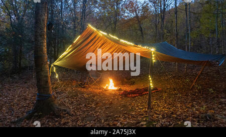 Primitive Tarp Tierheim mit Lagerfeuer und Lichterketten. Survival Bushcraft Setup in den Blue Ridge Mountains in der Nähe von Asheville. Stockfoto
