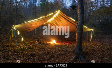 Primitive Tarp Tierheim mit Lagerfeuer und Lichterketten. Survival Bushcraft Setup in den Blue Ridge Mountains in der Nähe von Asheville. Stockfoto