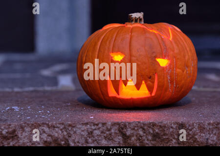 Lächelnd und glänzende Halloween Kürbis in der Dunkelheit auf dem Boden liegen. In Deutschland, in Bayern, im Oktober. Stockfoto