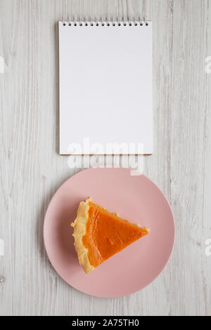 Hausgemachte Thanksgiving Kürbiskuchen auf einem rosa Platte, leer Notebook auf einem weißen Holz- Oberfläche, Ansicht von oben. Overhead, von oben, flach. Kopieren Sie Platz. Stockfoto