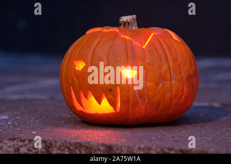 Lächelnd und glänzende Halloween Kürbis in der Dunkelheit auf dem Boden liegen. In Deutschland, in Bayern, im Oktober. Stockfoto