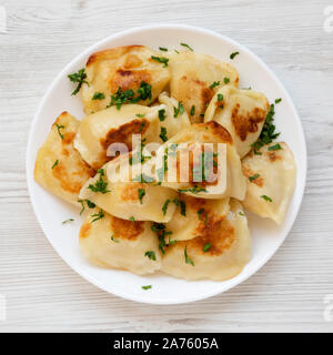 Hausgemachte, traditionelle polnische gebraten Kartoffel pierogis auf einem weißen Teller auf einem weißen Holz- Oberfläche, Ansicht von oben. Von oben, flach und Overhead. Nahaufnahme. Stockfoto