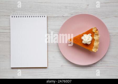 Hausgemachte Thanksgiving Kürbiskuchen auf einem rosa Platte, leere Notepad auf weißem Holz- Oberfläche, Ansicht von oben. Ansicht von oben, von oben, flach. Kopieren Sie Platz. Stockfoto