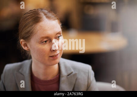 Junge rothaarige Frau in Jacke an Treffen im Cafe sitzen Stockfoto