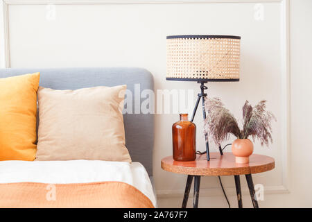 Stilvolle Lampe auf hölzernen Nachttisch neben Blume im großen Glas Vase in skandinavischen Schlafzimmer Innenraum Stockfoto