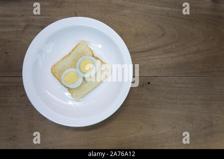 Die Hälfte geschnitten hart gekochte Ei auf getoastetes Sandwich Brot, bereit zu essen, in weiße Platte, hölzernen Tisch Hintergrund Stockfoto