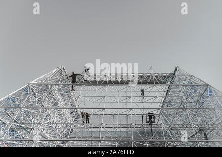 Geometrische Struktur, Stahlrahmen, Farbe silber, Hochbau mit Silhouetten der unkenntlich Arbeiter auf Himmel Hintergrund. Moderne Hintergrund Stockfoto