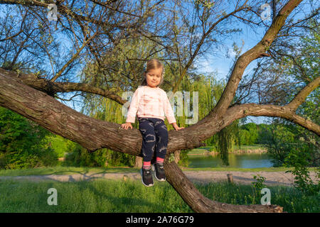 Kleine niedliche Mädchen sitzen auf Baum im Sommer Tag Stockfoto