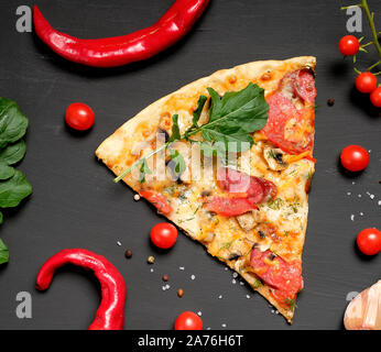 Dreieckige Stück Pizza mit Pilzen, geräucherte Wurst, Tomaten und Käse, schwarzer Hintergrund, flach Stockfoto