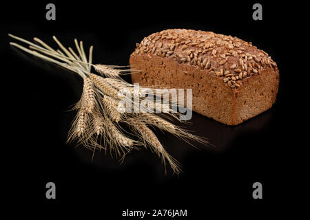 Lecker dunkles Brot mit Sonnenblumenkernen und trockene Ohren von Weizen. Zutaten für die Herstellung von Sandwiches auf einen dunklen Tisch. Schwarzen Hintergrund. Stockfoto