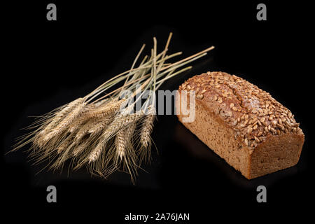 Lecker dunkles Brot mit Sonnenblumenkernen und trockene Ohren von Weizen. Zutaten für die Herstellung von Sandwiches auf einen dunklen Tisch. Schwarzen Hintergrund. Stockfoto