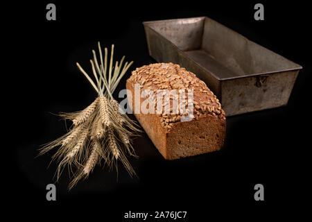Lecker dunkles Brot mit Sonnenblumenkernen und trockene Ohren von Weizen. Zutaten für die Herstellung von Sandwiches auf einen dunklen Tisch. Schwarzen Hintergrund. Stockfoto