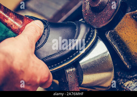 Die Hände eines erfahrenen Schuster in einer Schuhfabrik arbeitet, Endbearbeitung, die Sohlen der Schuhe, an einer Maschine Stockfoto