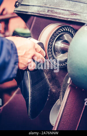 Die Hände eines erfahrenen Schuster in einer Schuhfabrik arbeitet, Endbearbeitung, die Sohlen der Schuhe, an einer Maschine. Stockfoto