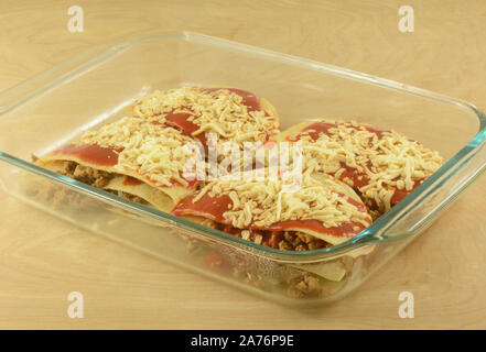 Abendessen Vorbereitung der Boden Schweinefleisch Enchiladas mit geriebenem Käse in Glas Auflaufform Stockfoto