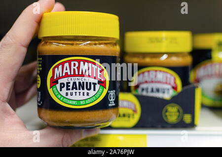 Marmite Erdnussbutter jar halten Sie in einer Hand neben dem Regal mit den anderen Gläsern. Traditionelle englische Produkt der Hefe. Stockfoto