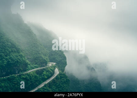 Durch niedrige Wolken und Nebel gefährlich scharfe Kurven auf der kurvenreichen Straße von 99 wendet sich an die Spitze der Tianmen Mountain, Zhangjiajie Nationalpark, Hu abgedeckt Stockfoto