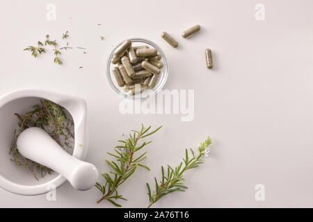 Mörtel mit Kräuter für die Verarbeitung natürlicher Kapseln auf weißer Tisch. Alternative natürliche Medizin Konzept. Ansicht von oben. Horizontale Komposition. Stockfoto