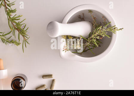 Mörtel mit Kräuter für die Verarbeitung natürlicher Kapseln auf weißer Tisch. Alternative natürliche Medizin Konzept. Ansicht von oben. Horizontale Komposition. Stockfoto