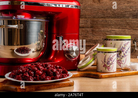 Rot Mixer, Sauerkirschen und Behälter Gläser für Mehl und Zucker mit einem braunen Tuch Stockfoto