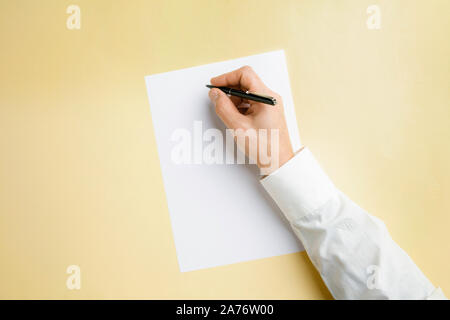 Männliche Hand mit Stift und schreiben auf leeres Blatt auf gelbem Hintergrund für Text oder Design. Leere Vorlagen für Kontakt, Werbung oder für den Einsatz in Unternehmen. Finanzen, Büro, Einkäufe. Mock up. Copyspace. Stockfoto